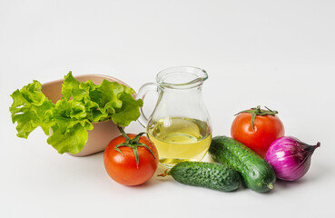 On a white background are ingredients for a vegetarian salad. Oil, tomatoes, cucumbers, red onions and lettuce are the basis of a healthy dish