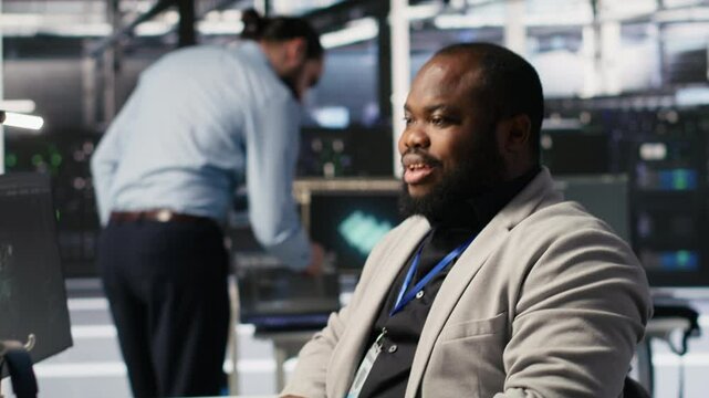 Satisfied data center employee finishing system maintenance on supercomputers. Smiling technician pleased by successful AI model training results on PC while overseeing server infrastructure, camera A