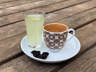 Traditional Turkish coffee served with lemon water and raisins on white saucer over rustic wooden table