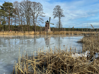 A pond with an island on which there is an old windmill and the surface of the pond water is...