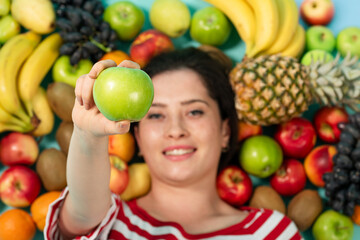 Fototapeta na wymiar Portrait of a young brunette woman lying near fruits and holding green apple in her hands.