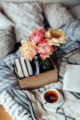 basket with a bouquet of pink and yellow peonies and books and a cup of tea on the bed