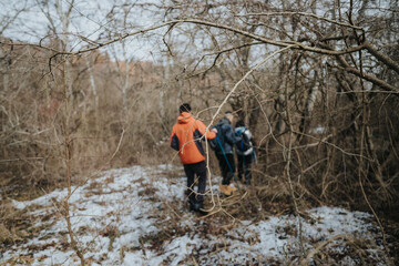 A group of people navigates through a winter forest with barren trees and traces of snow, showcasing the spirit of exploration, resilience in nature, and outdoor adventure during the colder season.