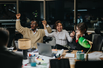 A group of multiracial coworkers cheerfully celebrate late at night after a productive meeting. They hold hands and express joy, showcasing teamwork and collaboration in a modern office setting.