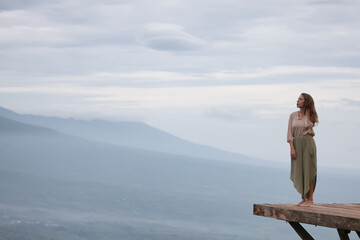 A girl is meditating, standing on a platform in the mountains, against the backdrop of a landscape of distant blurred mountains