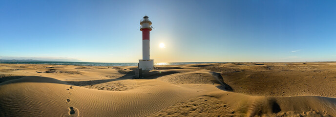 Lighthouse overlooking sandy beach at sunrise.