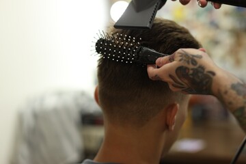 Professional barber blow drying client's hair in barbershop, closeup. Space for text