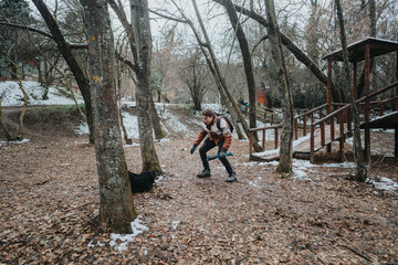 Fototapeta premium A person playing with a dog in a forest during a cold winter day, showcasing friendship and outdoor enjoyment in a natural setting.