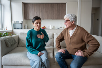 Senior couple faces health scare, woman struggles with tight chest and dizziness of heart attack or panic attack. Anxiety rapid heartbeat tension, helpless husband worries and want to call emergency