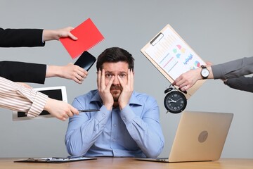 Man overwhelmed by different requests from colleagues at desk on light grey background