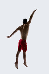 Athletic male swimmer in red swimwear glides with extended arm and streamlined posture during freestyle technique against white studio background. Concept of sport, motion, training, control
