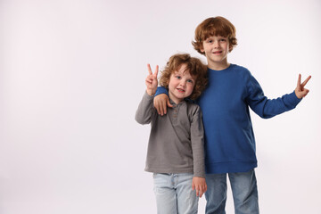 Cute little brothers showing V-signs on white background. Space for text