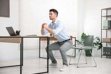 Handsome man doing exercise near desk in office