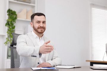 Happy recruiter offering handshake at desk in office, space for text