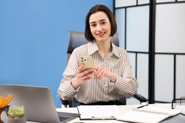 Smiling secretary using smartphone while working at table in office