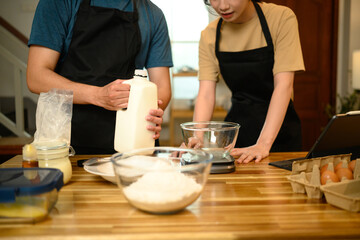 Cheerful young couple preparing pancake batter together in kitchen