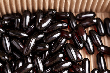 Dark brown Omega 3 softgel capsules in cardboard box close up. Top view. 