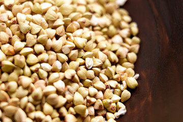 Raw buckwheat grains in brown wooden bowl. Uncooked organic dried ingredient. Macro shot. Top view. 