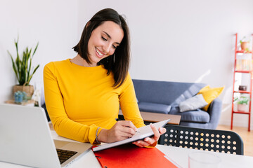Happy young student woman taking notes while listening on virtual training class. Millennial female...