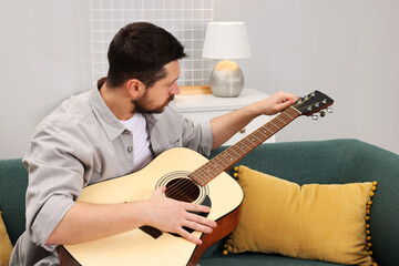 Relaxing hobby. Man playing guitar on sofa at home