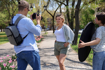 Professional photographers with reflector and camera near model during shooting outdoors on sunny...