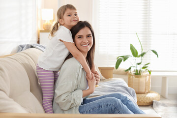 Happy mother and her cute daughter on sofa at home