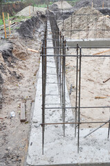 Strip foundation construction close up. House concrete foundation with reinforced footing trenches, rebars installed and concrete poured.