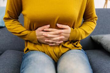 Woman experiencing abdominal pain, holding hands on stomach, suffering from gastritis, menstrual period cramps or digestive problems. Menstruation, stomach ache, period concept
