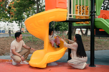 Joyful little girl enjoys sliding with support from her loving parents on both sides