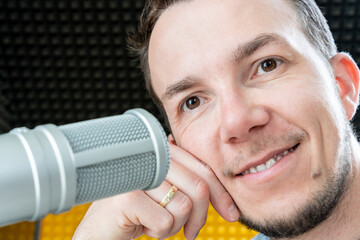 Man leaning on hand smiling beside professional microphone in studio, visualizing positive mood in...