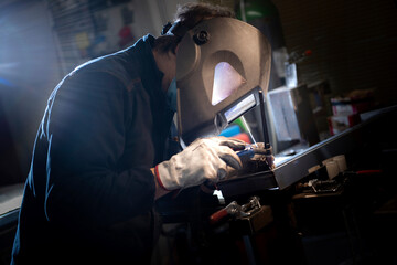 Skilled worker welding metal in a workshop, wearing protective helmet and gloves. Industrial scene with bright lighting and sparks. Manual labor and safety in metal fabrication