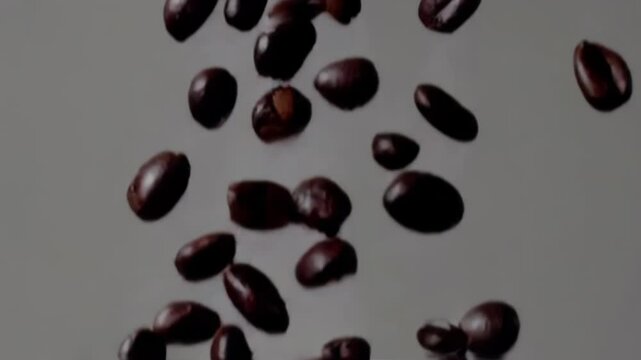 Roasted coffee beans falling in slow motion on grey background, close-up macro view