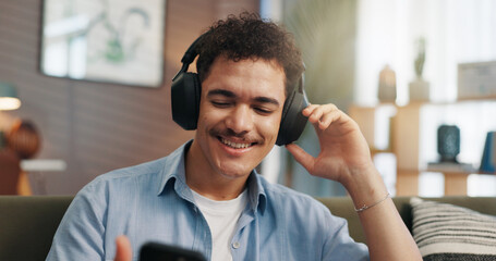 Obraz premium Headphones, man and happy with phone in home for streaming service, feel good playlist and audio subscription. Relax, person and internet connection on sofa for watching online video and social media