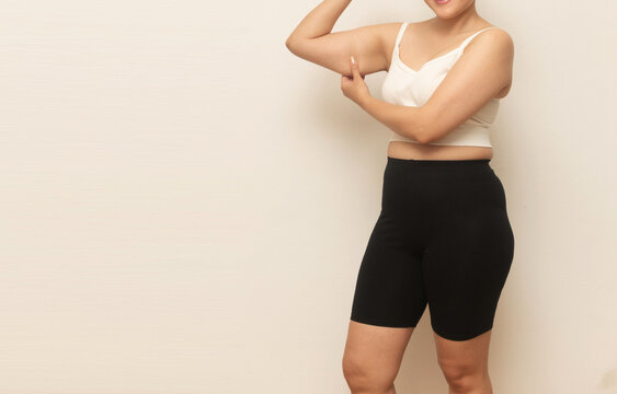 Midsection of a woman in workout clothes pinching underarm fat, highlighting loose skin or flabby triceps for fitness concept