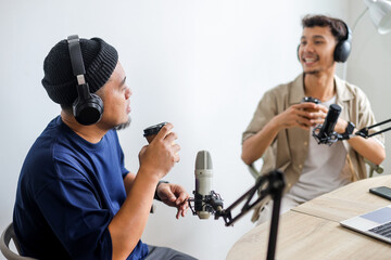 Cheerful Young Man Co-hosting an Audio Broadcast with a Guest While Drink Coffee
