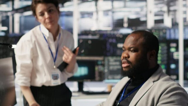Lead data center admin overseeing IT expert integrating AI in equipment rigs. African american employee under server farm team leader supervision using deep learning for operational tasks, camera A
