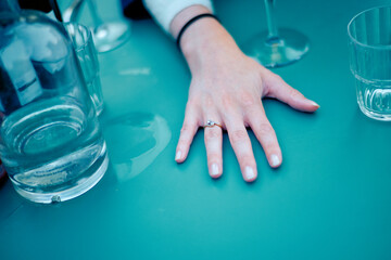 Hand with an engagement ring on a teal table surrounded by glasses. Brussels, Belgium