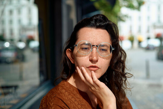 Woman with large glasses gazes thoughtfully outside a cafe window. Brussels, Belgium