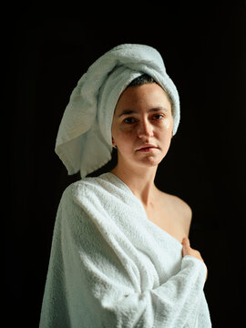 Woman wrapped in towel with a towel on head against a dark background.