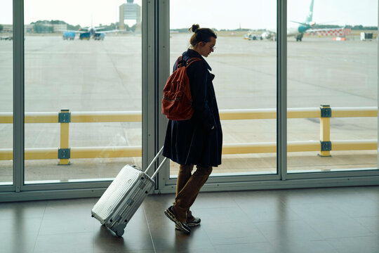 Woman at airport terminal with luggage near large windows overlooking the runway.