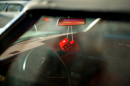 Red fuzzy dice hang from the rear-view mirror of a vintage car, sunlight dapples the interior. New York City, USA