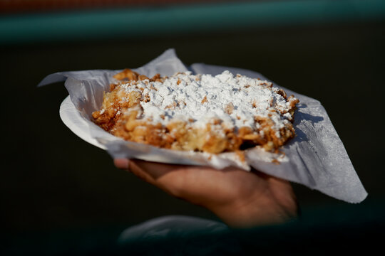 Hand holds a plate with fried apple crumble dessert covered in powdered sugar outdoors. New York City, USA