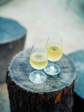 Two glasses of white wine on a round wooden surface outdoors.