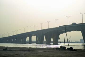 A long concrete bridge stretches across a calm river under a hazy sky. Abu Dhabi, UAE