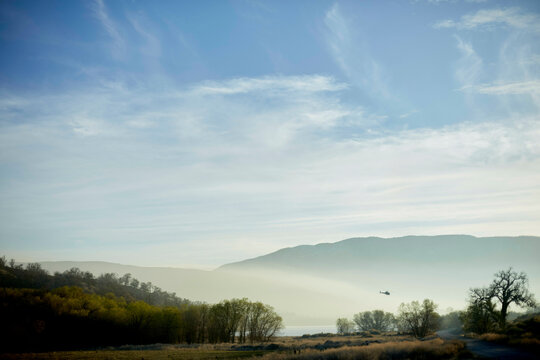 Helicopter flies over serene landscape with hills, trees, and a misty sky. Los Angeles, USA