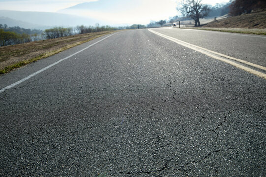 A winding road stretches into the distance with cracked asphalt and a misty landscape. Los Angeles, USA