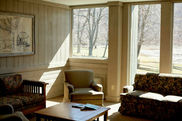 Sunlit cozy living room with armchairs, sofa, and a coffee table by large windows. Road Trip USA