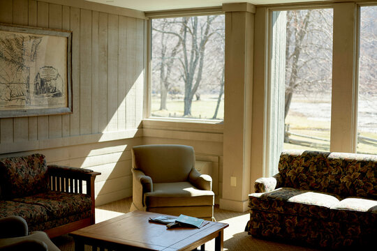 Sunlit cozy living room with armchairs, sofa, and a coffee table by large windows. Road Trip USA