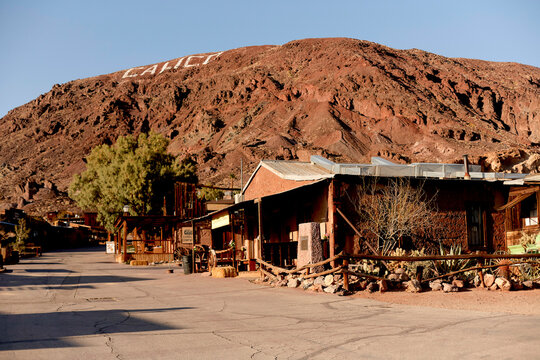 Desert town with rugged buildings and a hillside displaying large white letters under clear sky. Road Trip USA