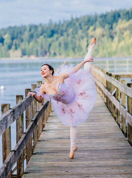 Ballerina performing an elegant arabesque on a wooden pier by a serene lake. WA, USA